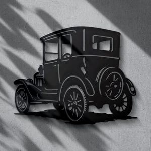 Könnte beinhalten: Schwarze Metall-Wandkunst, die ein Oldtimer-Auto darstellt. Das klassische Automobil weist ein detailliertes Design von Karosserie, Rädern und anderen Komponenten auf. Das Auto ist an einer strukturierten grauen Wand befestigt, mit Schatten von Blättern.