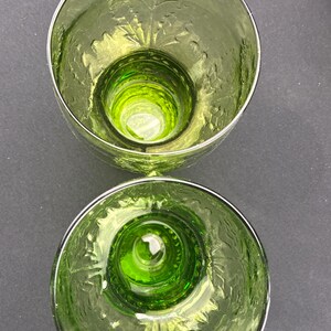 Puede incluir: Dos vasos de vidrio te&ntilde;ido de verde con un patr&oacute;n floral grabado en los lados. Los vasos tienen una base gruesa y un borde plateado. El interior de los vasos es de color verde vibrante.
