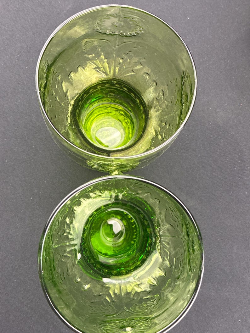 Puede incluir: Dos vasos de vidrio te&ntilde;ido de verde con un patr&oacute;n floral grabado en los lados. Los vasos tienen una base gruesa y un borde plateado. El interior de los vasos es de color verde vibrante.