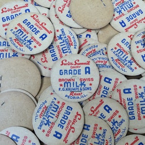 May include: A close-up of a pile of vintage milk bottle caps. The caps are round and made of cardboard. They are printed with the words "Swiss Summit Dairy Grade A Brown Swiss Milk" and "F.G. Krumpe & Sons Peoria, Ill. Raw".