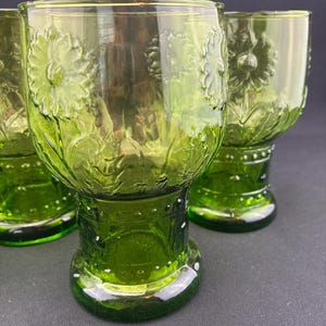 Puede incluir: Cuatro vasos para beber te&ntilde;idos de verde. Cada vaso presenta un dise&ntilde;o floral en relieve y una base. Los vasos est&aacute;n hechos de un material transparente, que permite el paso de la luz. Los vasos est&aacute;n dispuestos sobre una superficie oscura.