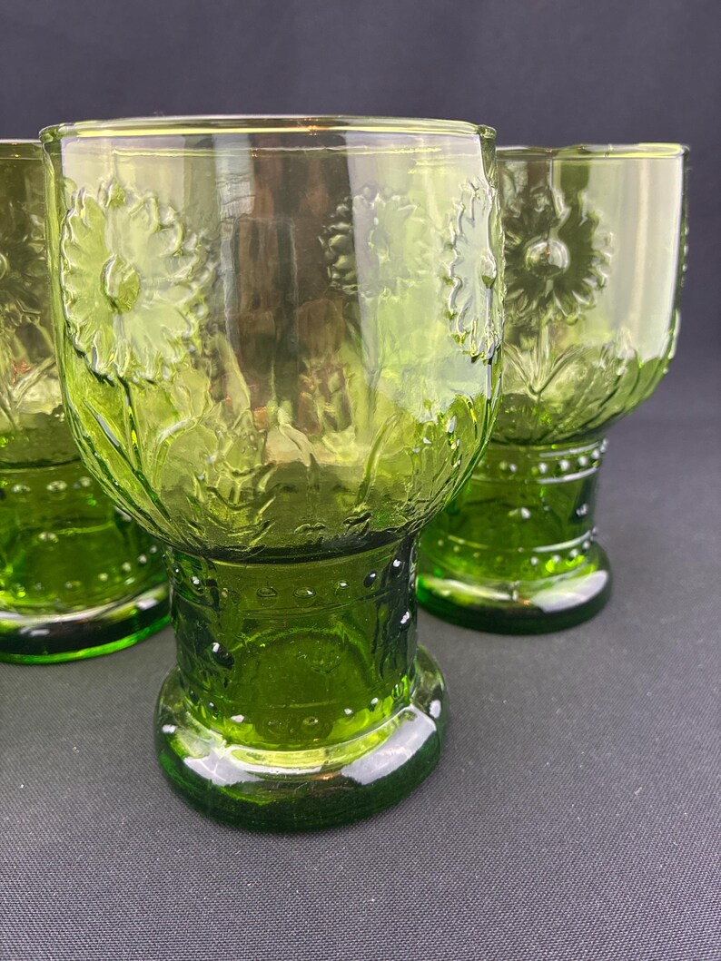Puede incluir: Cuatro vasos para beber te&ntilde;idos de verde. Cada vaso presenta un dise&ntilde;o floral en relieve y una base. Los vasos est&aacute;n hechos de un material transparente, que permite el paso de la luz. Los vasos est&aacute;n dispuestos sobre una superficie oscura.