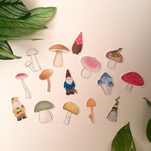Puede incluir: Un conjunto de 13 pegatinas de setas y gnomos de colores. Las pegatinas presentan varios dise&ntilde;os de setas, incluyendo setas rojas y blancas con lunares, setas marrones con lunares blancos y setas azules con lunares blancos. Tambi&eacute;n hay dos pegatinas de gnomos, una con un gorro rojo y otra con un gorro azul.