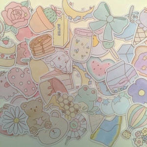 May include: A collection of pastel-colored stickers featuring various cute designs, including a watermelon, a frog, a bunny, a bear, a jar of fireflies, a slice of cake, a pot of cactus, a crescent moon, a heart, a honeycomb, a pair of boots, a hot air balloon, and a blueberry carton. The stickers are perfect for adding a touch of whimsy to journals, planners, laptops, and other items.