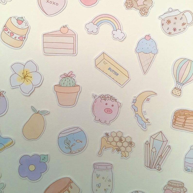 May include: A collection of colorful stickers featuring various designs, including a rainbow, a pig, a cactus, a pear, a fishbowl, a honeycomb, a crystal, a moon, a jar, a cupcake, a heart, a butterfly, a cloud, a pancake, a bottle of butter, a flower, a jar, and a teacup.