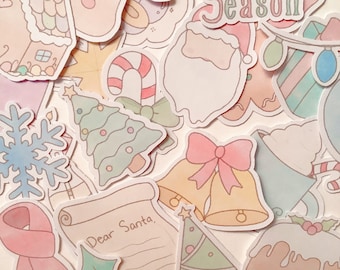 Puede incluir: Una colección de pegatinas navideñas en colores pastel. Los diseños incluyen una casa de jengibre, Papá Noel, un árbol de Navidad, un bastón de caramelo, campanas, una bufanda y una carta que dice "Dear Santa". También se ve el texto "It's the Season".