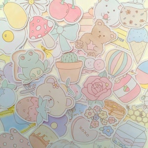 May include: A collection of pastel-colored stickers featuring various cute designs, including a frog, a bear, a cactus, a heart, a rose, a strawberry, a hot air balloon, a honey pot, and a blueberry container. The stickers are perfect for adding a touch of whimsy to journals, planners, and other craft projects.
