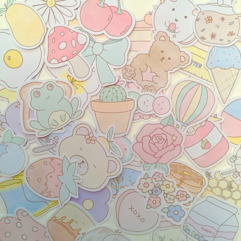 May include: A collection of pastel-colored stickers featuring various cute designs, including a frog, a bear, a cactus, a heart, a rose, a strawberry, a hot air balloon, a honey pot, and a blueberry container. The stickers are perfect for adding a touch of whimsy to journals, planners, and other craft projects.