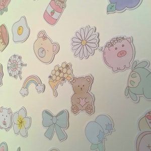 May include: A collection of colorful stickers featuring various cute designs, including a bear, a pig, a flower, a honeycomb, a rainbow, and a jar of jam. The stickers are perfect for adding a touch of whimsy to journals, planners, laptops, and other surfaces.