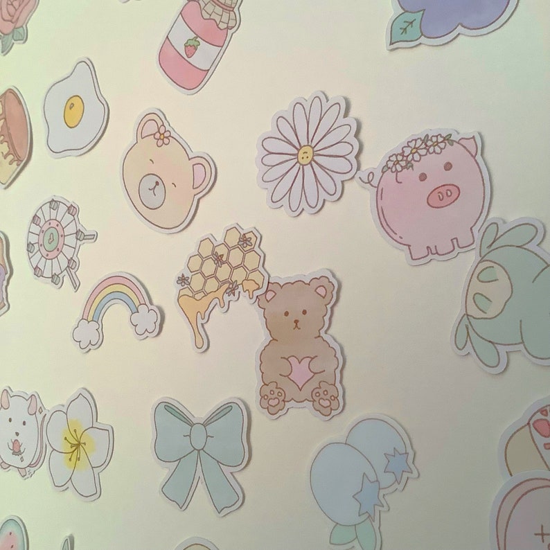 May include: A collection of colorful stickers featuring various cute designs, including a bear, a pig, a flower, a honeycomb, a rainbow, and a jar of jam. The stickers are perfect for adding a touch of whimsy to journals, planners, laptops, and other surfaces.
