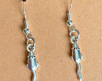 May include: A pair of silver-coloured mouse-shaped dangle earrings. Each earring features a mouse charm with small eye details and a curved tail, suspended from a hook with a coiled design.