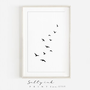 Peut inclure: Une impression minimaliste en noir et blanc d'un vol d'oiseaux en ligne diagonale. L'impression est encadr&eacute;e dans un cadre blanc.