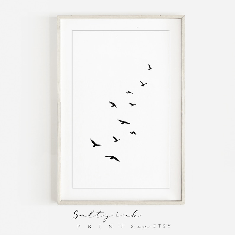 Peut inclure: Une impression minimaliste en noir et blanc d'un vol d'oiseaux en ligne diagonale. L'impression est encadr&eacute;e dans un cadre blanc.