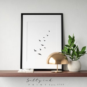 Peut inclure: Impression minimaliste en noir et blanc d'un vol d'oiseaux en formation de V. L'impression est encadr&eacute;e dans un cadre noir et est expos&eacute;e sur une &eacute;tag&egrave;re avec une lampe dor&eacute;e et une plante en pot.