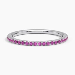 May include: A silver ring with a band of small, bright pink gemstones. The ring is set against a white background, highlighting the gemstones' vibrant color and the ring's polished finish. A delicate piece of jewelry.