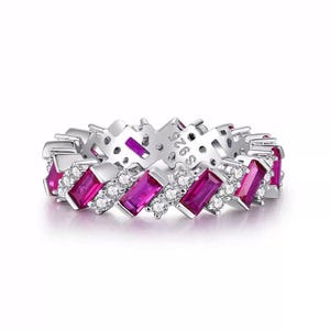 Puede incluir: Un anillo de tono plateado con un patrón repetitivo de piedras rectangulares de color rosa vibrante en corte baguette, alternadas con pequeñas piedras redondas transparentes. El interior tiene grabado S925, indicando la composición.