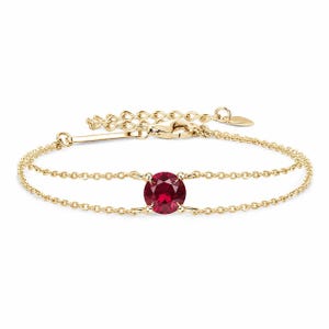 May include: A delicate gold chain bracelet featuring a single round, faceted deep red gemstone set in the center. The bracelet has a double-strand design connected by the stone, a lobster claw clasp, and an adjustable extender chain with a small tag.