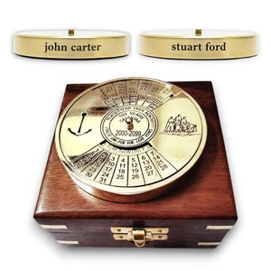 Puede incluir: Un calendario perpetuo de latón con una caja de madera. El dial del calendario muestra los años 2000-2099, los meses y los días. Dos placas de latón con los nombres "john carter" y "stuart ford".