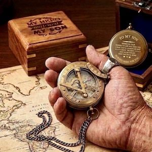 May include: A brass sundial compass with a chain and a hinged lid featuring the engraved text TO MY SON, WHEREVER YOUR JOURNEY IN LIFE MAY TAKE YOU, I PRAY YOU'LL ALWAYS BE SAFE, ENJOY THE RIDE, AND NEVER FORGET YOUR WAY BACK HOME, ALWAYS HERE FOR YOU.