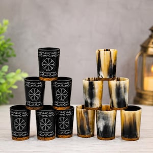 以下が含まれることがあります： 2つのスタックに配置された12個のドリンクカップ。6個は黒色で、白色のコンパスのシンボルが刻印されており、コルクの底が付いています。6個は天然の角で作られており、黒とクリーム色の縦縞模様で、コルクの底が付いています。