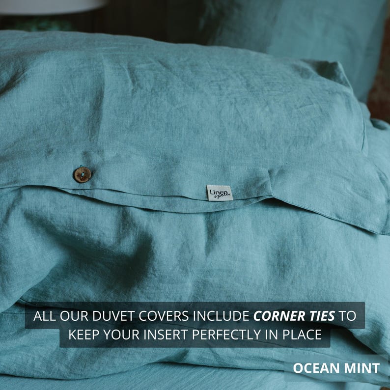 May include: Close-up of a duvet cover in ocean mint color. The fabric has a textured appearance with a button closure and a small label that says "Linen.". The text on the image says "ALL OUR DUVET COVERS INCLUDE CORNER TIES TO KEEP YOUR INSERT PERFECTLY IN PLACE".