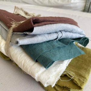 May include: A stack of fabric swatches in various colors, including brown, gray, teal, white, and green. The fabric is folded and arranged in a pile.