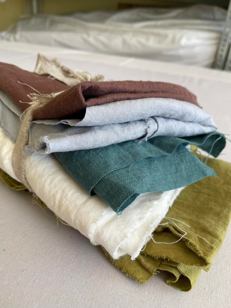 May include: A stack of fabric swatches in various colors, including brown, gray, teal, white, and green. The fabric is folded and arranged in a pile.