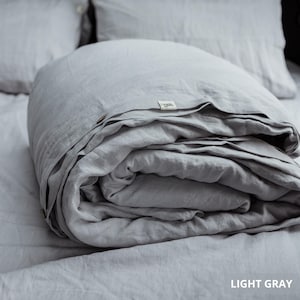 May include: A light gray linen duvet cover folded on a bed, with two matching pillows in the background. The duvet cover has a tag that reads "Linen." The text "LIGHT GRAY" is visible in the bottom right corner.