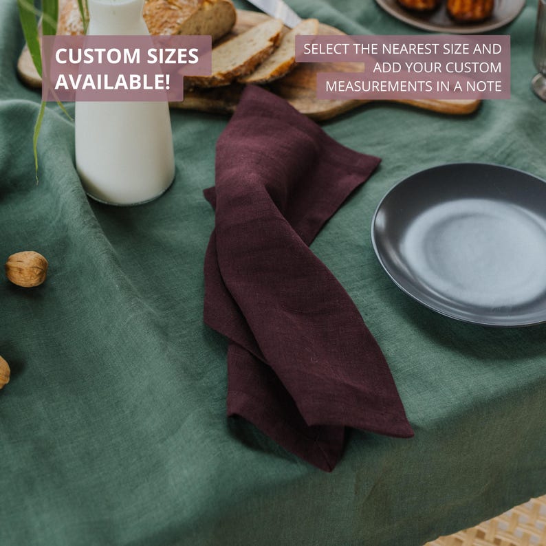 May include: A burgundy linen napkin is folded on a green tablecloth, next to a dark gray plate. A white bottle and bread are in the background. Text on the image reads: "CUSTOM SIZES AVAILABLE!" and "SELECT THE NEAREST SIZE AND ADD YOUR CUSTOM MEASUREMENTS IN A NOTE."