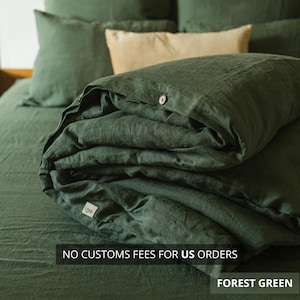 May include: Forest green linen bedding set, including a duvet cover, pillowcases, and fitted sheet. The duvet cover is folded, showing a wooden button closure. The text "NO CUSTOMS FEES FOR US ORDERS" and "FOREST GREEN" are visible.