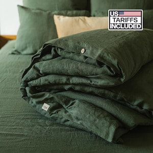 May include: A dark forest green duvet cover featuring a button closure with visible wooden buttons and a small white fabric label. The bedding set includes matching pillowcases and a beige accent pillow, with a US TARRIFS INCLUDED graphic.