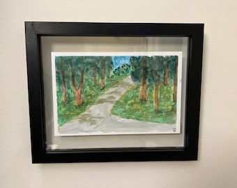 Puede incluir: Pintura a la acuarela de un camino sinuoso a través de un bosque, enmarcada en un marco negro rectangular. La obra presenta árboles verdes, un camino gris y un cielo azul. La pintura se exhibe en una pared blanca.