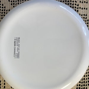 Puede incluir: Plato para hornear redondo de Corning Ware blanco de 16,5 cm de di&aacute;metro con asa. El plato est&aacute; marcado con "Corning Ware" y "Range Oven Microwave Corning NY. USA 479 MA".