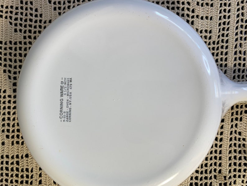 Puede incluir: Plato para hornear redondo de Corning Ware blanco de 16,5 cm de di&aacute;metro con asa. El plato est&aacute; marcado con "Corning Ware" y "Range Oven Microwave Corning NY. USA 479 MA".
