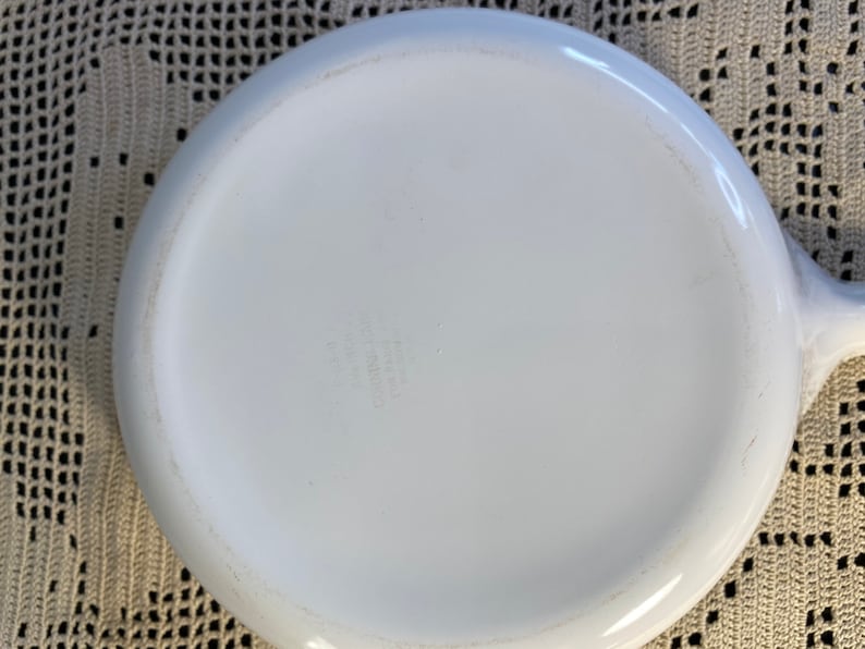 Puede incluir: Plato para hornear de cer&aacute;mica blanca con forma redondeada y un solo asa. El fondo del plato tiene una peque&ntilde;a inscripci&oacute;n descolorida.