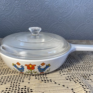 Puede incluir: Plato para hornear blanco con tapa de vidrio. El plato tiene un dise&ntilde;o floral azul y naranja con p&aacute;jaros.