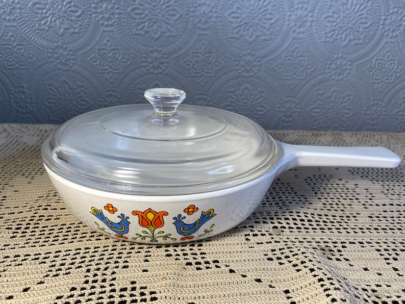 Puede incluir: Plato para hornear blanco con tapa de vidrio. El plato tiene un dise&ntilde;o floral azul y naranja con p&aacute;jaros.
