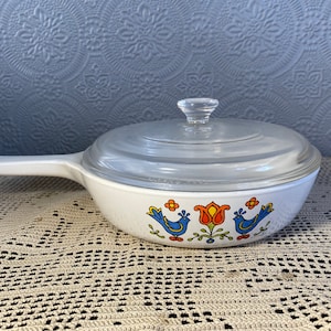 Puede incluir: Plato para hornear blanco con tapa de vidrio y un dise&ntilde;o floral azul y naranja con p&aacute;jaros.
