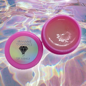 Puede incluir: Tarro de imprimación labial rosa con un logotipo de diamante negro y el texto "Diamante Cosmetics Lip Primer".