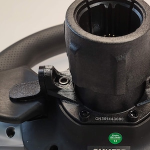 May include: A black Fanatec GT SW Pro racing wheel with a silver rim and black leather grip. The wheel has a black plastic center hub with a QR code and the text "GT SW Pro" and "S/N: GV481152510".