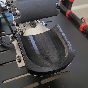 May include: A black metal foot pedal with a black plastic cover. The pedal is attached to a metal frame with screws.