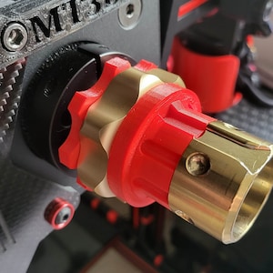 Puede incluir: Primer plano de un accesorio de cámara rojo y dorado impreso en 3D con el texto "MT3D" en el lateral. El accesorio está diseñado para sujetarse a un rig de cámara.