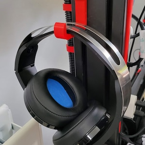 May include: Black headphones with blue ear cushions hanging on a red and black 3D printer stand.