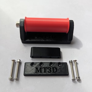 May include: A black 3D-printed bracket with a red cylindrical roller, a separate black rectangular mounting plate with the text MT3D, a small black spacer block, and four silver metal bolts with matching nuts for assembly and installation.