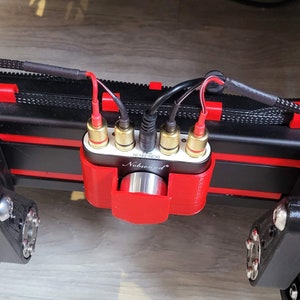 Op de afbeelding: Een rode 3D-geprinte behuizing met vergulde RCA-connectoren en een zwarte Nobsound DAC-2803-versterker. De behuizing is gemonteerd op een zwart oppervlak met rode accenten.