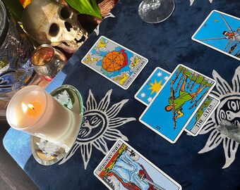 May include: A tarot card reading spread with four cards laid out on a blue fabric with a sun pattern. The cards are "The Star", "Wheel of Fortune", "King of Swords", and "The Star".