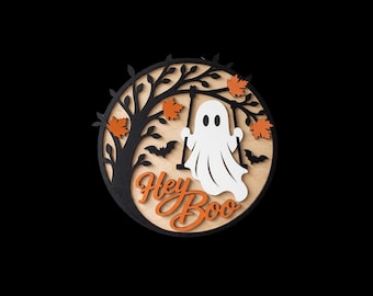 May include: A circular wooden wall sign featuring a layered design with a black tree silhouette, orange autumn leaves, and black bats. A white ghost figure sits on a swing suspended from the tree branches. The text Hey Boo is in orange.