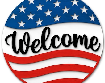 May include: A round wooden sign with a patriotic theme. The top section is blue with white stars, the middle is white, and the bottom has red and white stripes. The word "Welcome" is written in black script across the center.