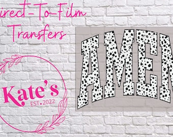 May include: A white and black dalmatian print iron-on transfer with the word "AMEN" in a bold, white font. The transfer is on a white brick background.