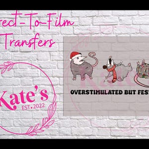 May include: A light grey graphic with three cartoon opossums in festive clothing. One wears a Santa hat, another a scarf, and the third is tangled in lights. Text reads "Overstimulated But Festive" and "Direct-To-Film Transfers". A pink logo says "Kate's EST.2022".